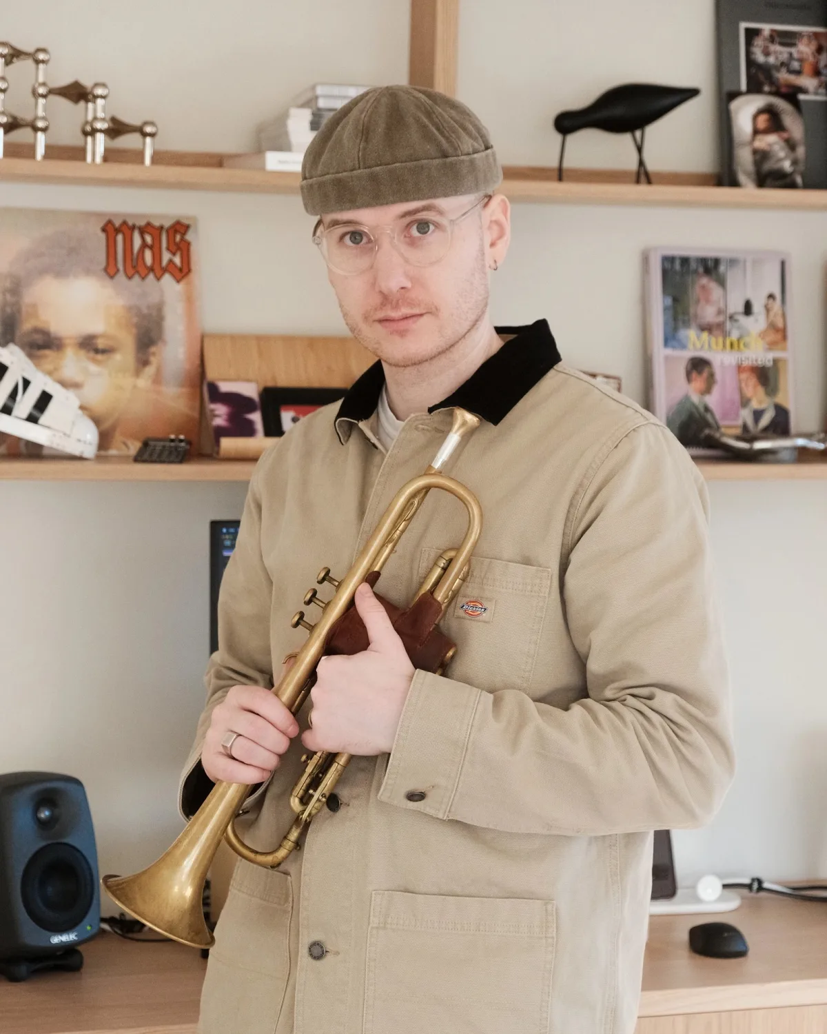 Kristoffer Eikrem holding his trumpet in the studio, records on the shelf behind him